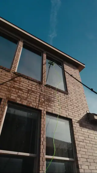 Water-fed pole brush cleaning upper windows on a brick Austin home