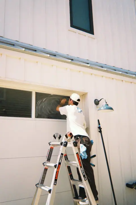 Crew member applying soap to residential window glass from a ladder