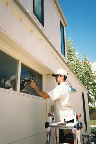 Crew member cleaning a bright residential window from a ladder