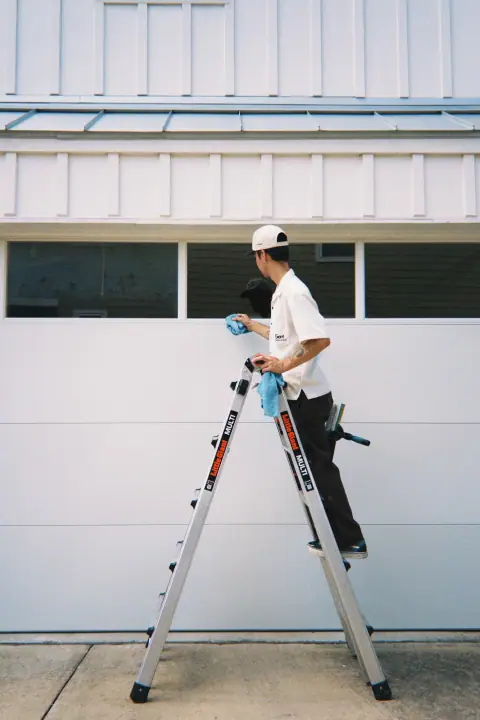 Giant Window Cleaning technician standing on a ladder while detailing a garage window