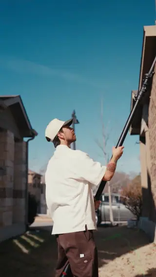 Crew member using an extension pole to clean upper exterior residential windows