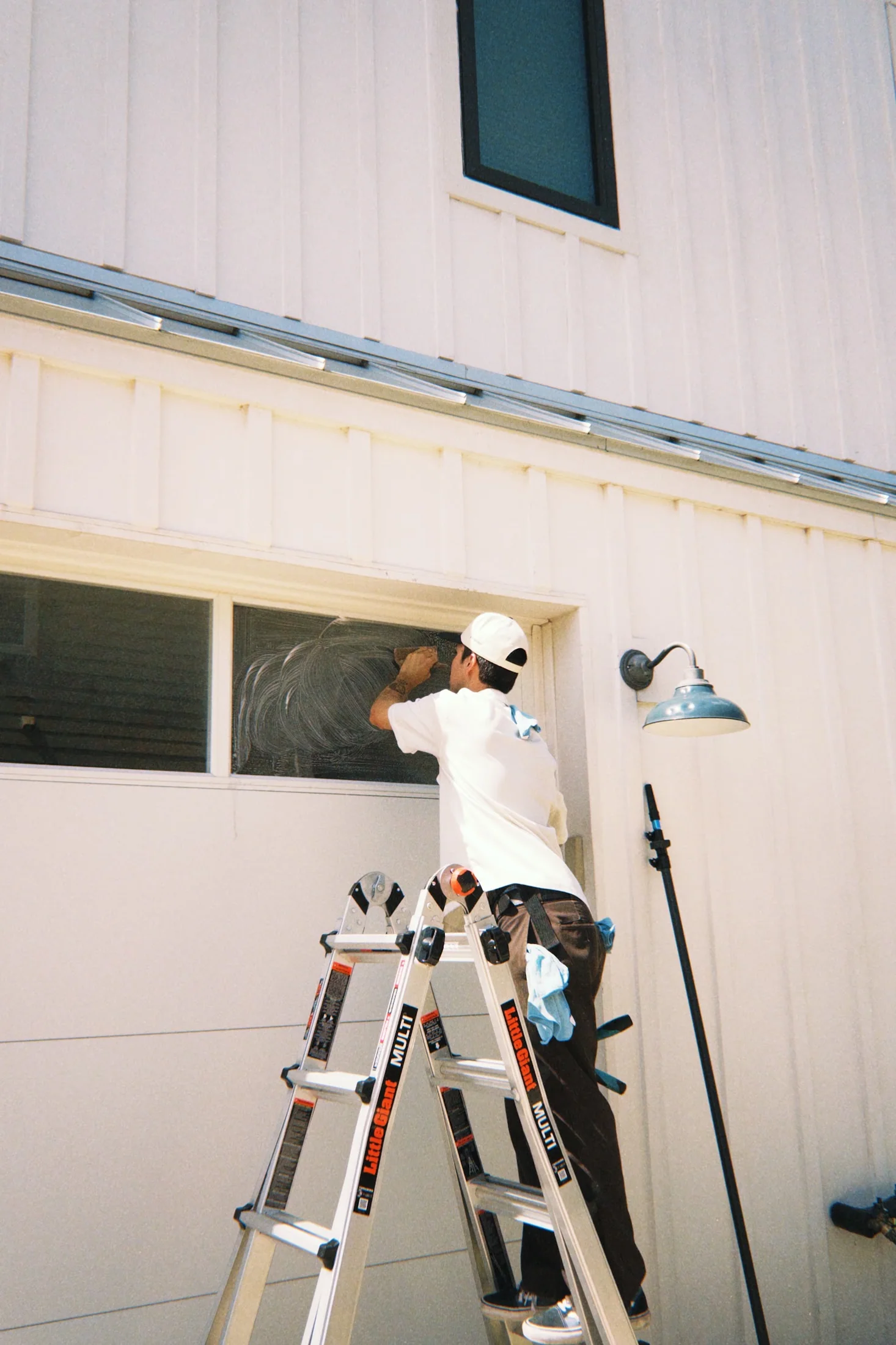 Crew member applying soap to residential window glass from a ladder