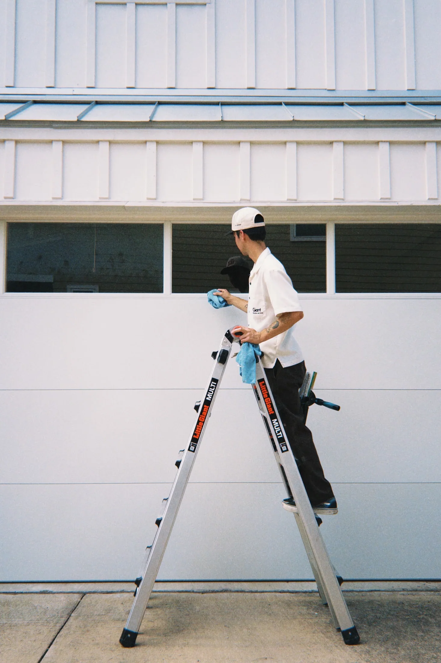 Giant Window Cleaning technician standing on a ladder while detailing a garage window